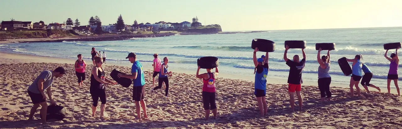 A group lifting sandbags overhead on the beach at sunrise